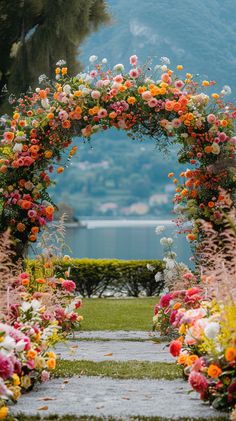 an arch made out of flowers on the side of a road with water in the background