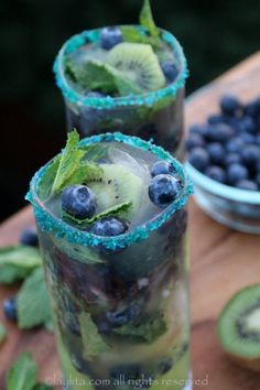 two glasses filled with blueberries and kiwis on top of a wooden table