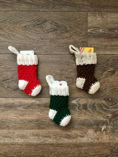 three crocheted christmas stocking hanging on a wooden floor, one is green, the other is red and white