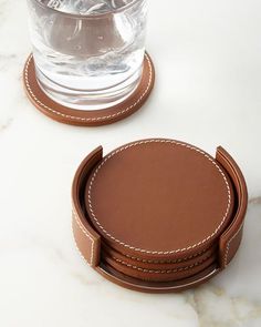 three coasters with stitching around the edges on a marble countertop next to a glass of water