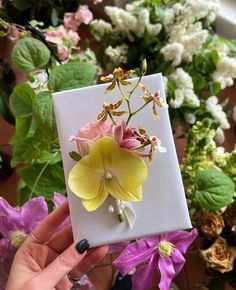 a person holding up a card with flowers on it in front of some other flowers