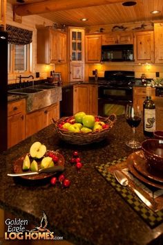 a bowl of fruit is sitting on the kitchen counter with wine glasses and silverware