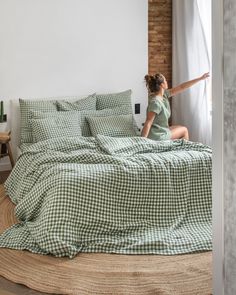 a woman sitting on top of a bed next to a green checkered comforter