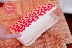 a hand holding a red and white case on top of a wicker place mat