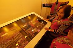 two women are looking at an old fashion jewelry display in a room with yellow walls