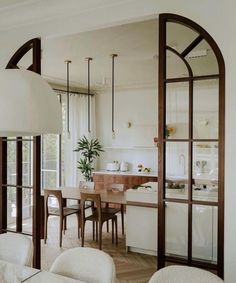 an open kitchen and dining room with white walls, wood flooring and large arched windows