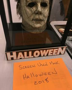 a halloween mask is on display in a glass case with an orange note attached to it