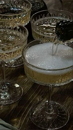 champagne being poured into wine glasses on top of a wooden table with other glassware