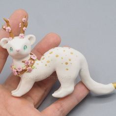 a hand holding a tiny white cat with gold spots on it's head and some pink flowers around its neck