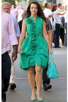 a woman in a green dress is walking down the street with a blue handbag