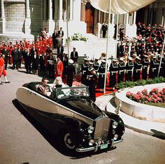 an old car driving down the street in front of a large group of men and women