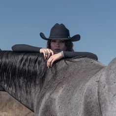 a woman wearing a cowboy hat leaning on a horse