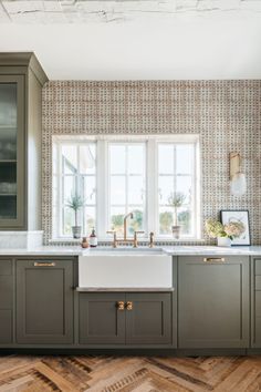 a kitchen with wooden flooring and green cabinetry next to a white sink in front of two windows