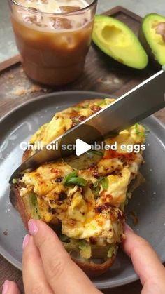 someone is cutting up an egg sandwich on a plate with avocado and coffee in the background