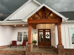 a white house with red chairs and a wooden front door on the side of it