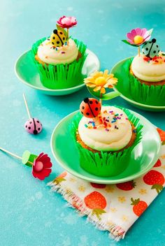 three cupcakes with white frosting and ladybug decorations on green plates