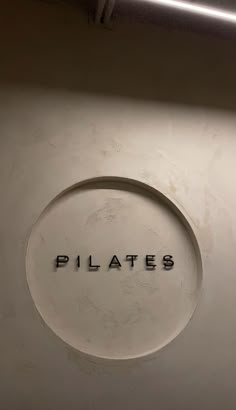 the word pilates written in black ink on a white wall with a circular hole