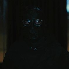 a man wearing glasses in the dark with his face covered by a black coat and hood