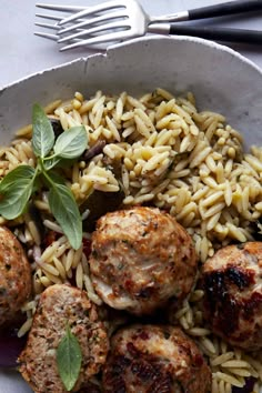 pasta with meatballs and vegetables in a white bowl on a table next to utensils