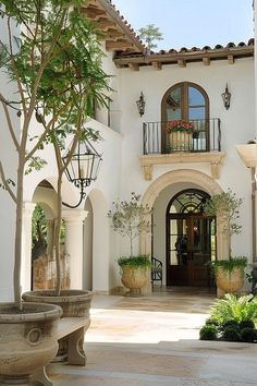 the front entrance to a large house with potted plants and trees on either side