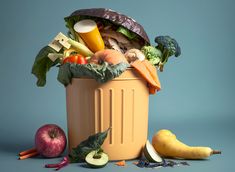 a trash can filled with vegetables and fruits on a blue background, next to an apple