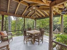 a covered patio with wooden furniture and lots of trees in the backgroung