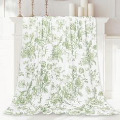 a green and white floral print curtain hanging from a fireplace mantel with candles in the background