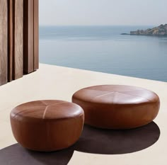 two brown leather stools sitting on top of a white floor next to the ocean