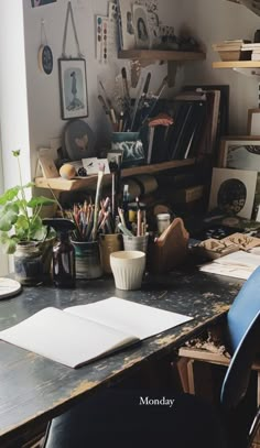 a desk with many items on it in front of a window and bookshelf