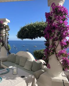 an outdoor seating area overlooking the ocean with purple flowers growing on it's pillars