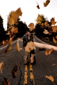 a man and woman standing in the middle of an empty road with leaves on it