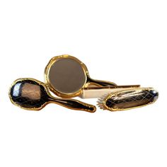 three different types of gold and black hair clips on a white surface with one being used as a mirror