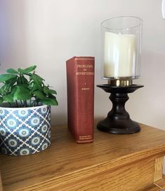 a candle and some books are sitting on a table next to a potted plant