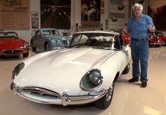 a man standing next to a white car in a showroom filled with old cars