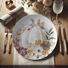 a white plate topped with a pumpkin surrounded by flowers and silverware next to napkins