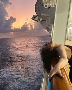 a woman leaning on the edge of a boat looking out at the ocean as the sun sets