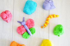 colorful play doughs laid out on a white wooden surface with toy worms and caterpillars