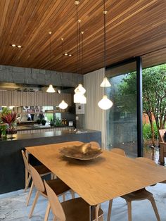 a dining room table and chairs in front of a kitchen with wood ceilinging, windows, and sliding glass doors