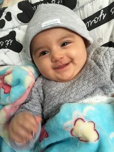 a baby laying on top of a bed wearing a gray hat and blue blanket with mickey mouse patches