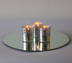 three silver candles sitting on top of a glass plate