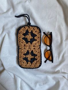 a crocheted bag with sunglasses on top of it next to a pair of glasses