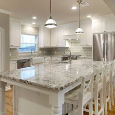 a large kitchen with white cabinets and marble counter tops, along with an island in the middle