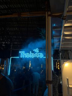 people standing in front of a neon sign that reads thaalasa on it at night