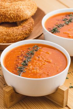 two bowls of tomato soup with bagels in the background