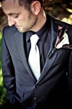 a man wearing a suit and tie with a flower in his lapel, looking down