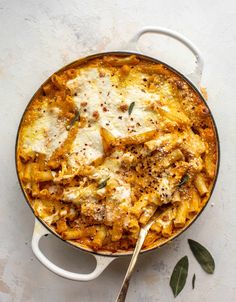 a pot filled with pasta and cheese on top of a white table next to a spoon