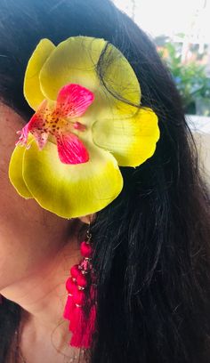 a woman with long black hair wearing yellow and pink flowers in her earrings