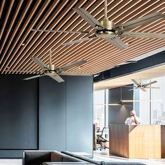 a man is sitting at a desk in the middle of a room with wooden ceiling fans