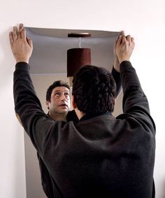 a man standing in front of a mirror holding his hands up to the ceiling light