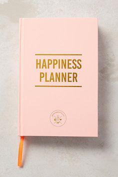 a pink notebook with the words happiness planner written on it and an orange pencil sticking out